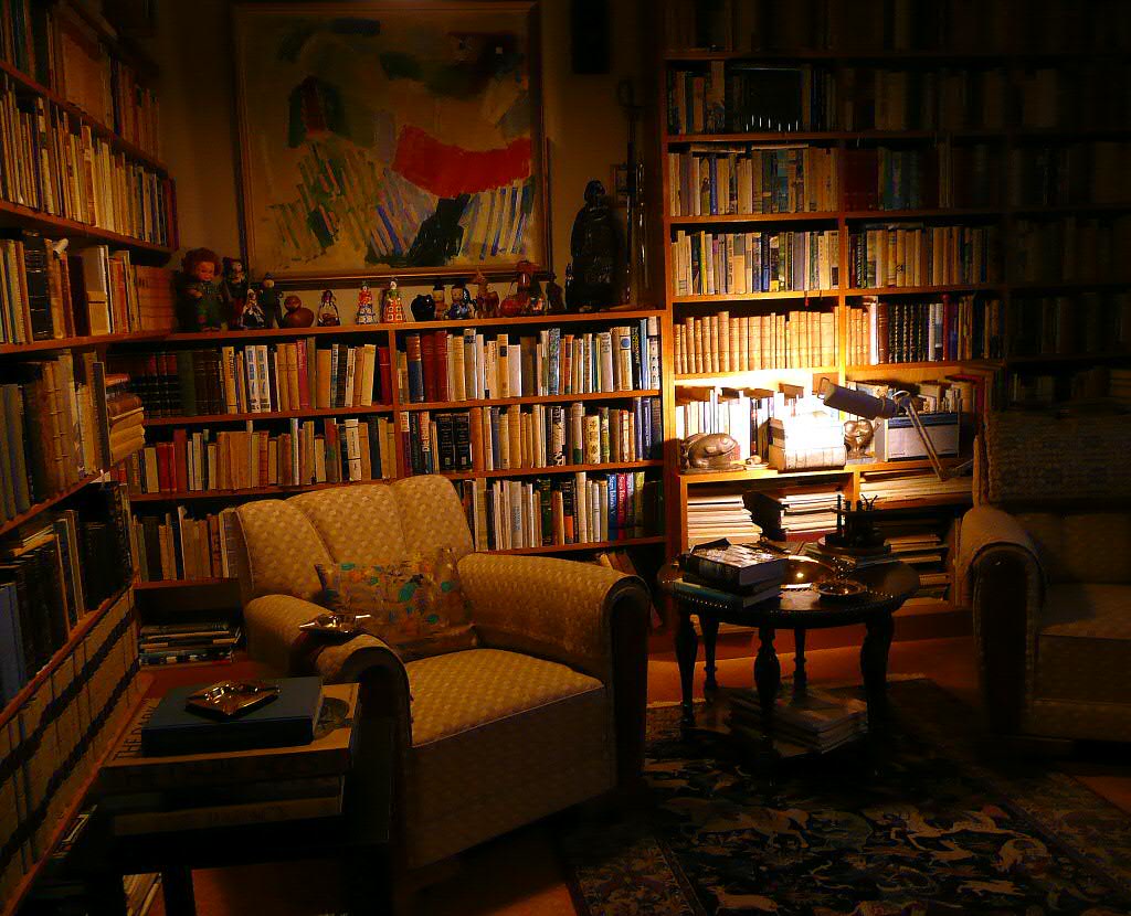 A cozy private reading room with floor-to-ceiling bookshelves, armchairs, and a lit side table lamp