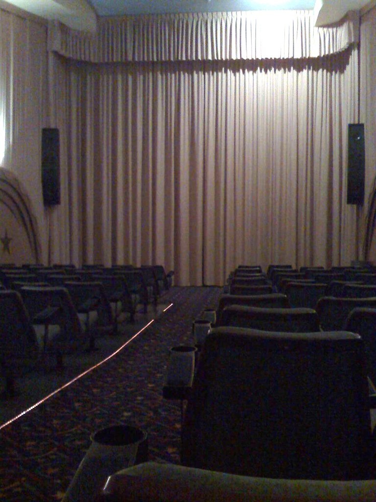 A closed curtain hangs over the stage above rows of empty seats at The Regal Theatre before a show